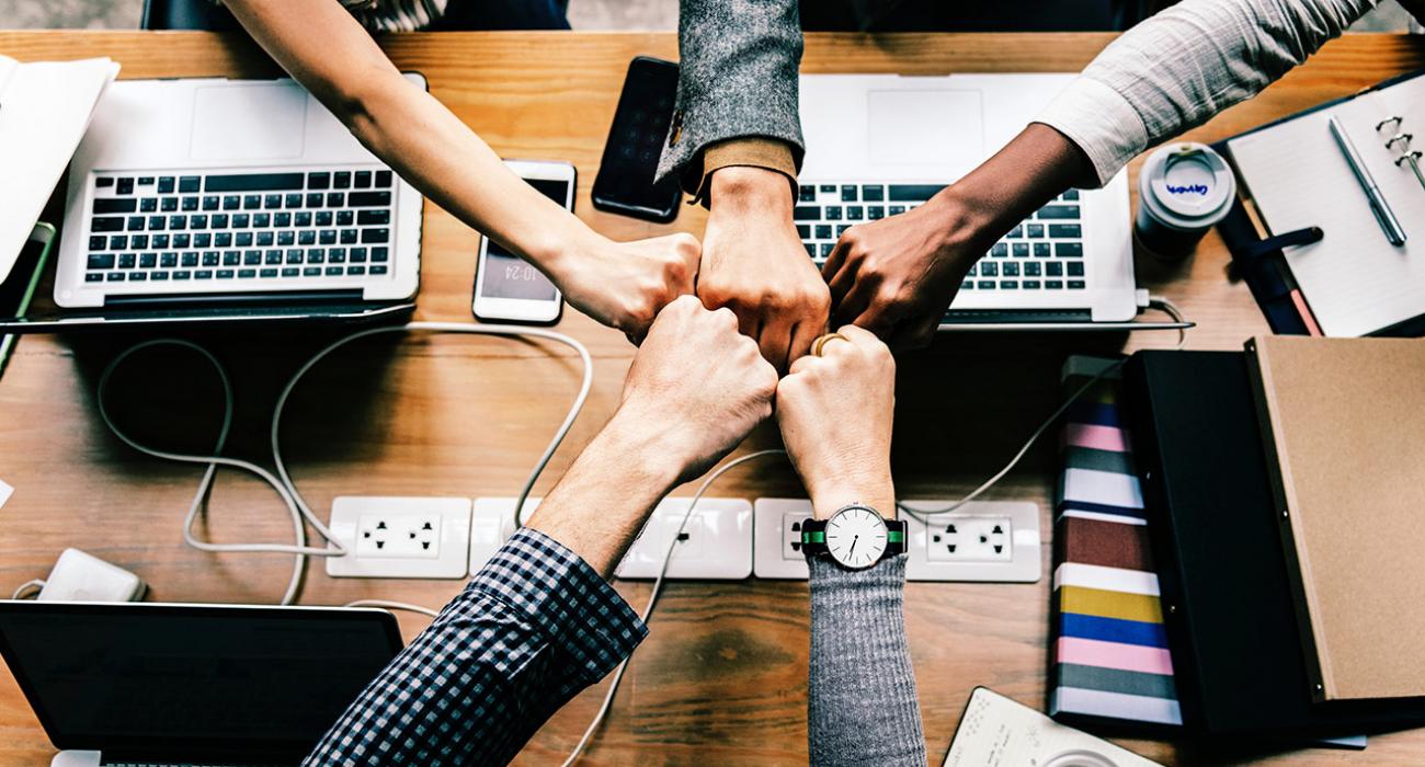 Diverse group of people fist bumping across a desk covered in laptops